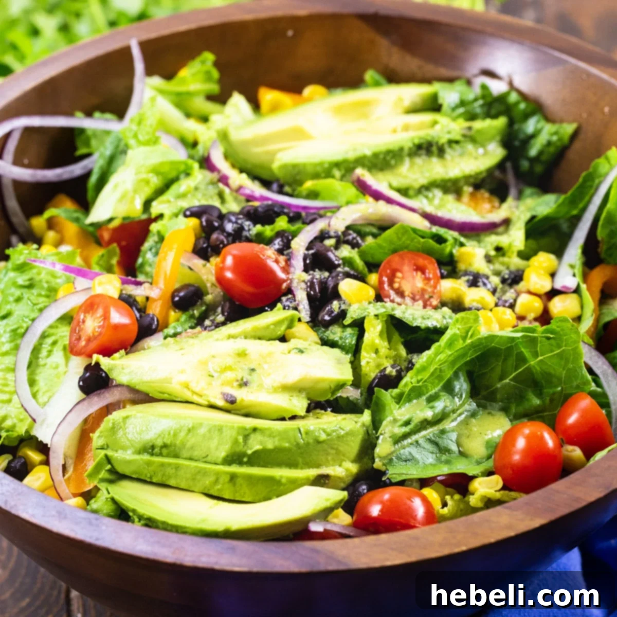 Large wooden salad bowl filled with Southwestern Salad featuring avocado slices, corn, black beans, bell peppers, and fresh greens.