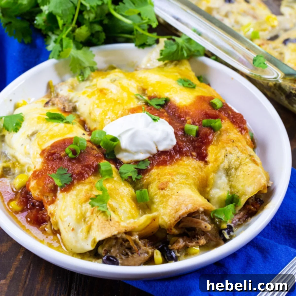 Three Pulled Pork Enchiladas topped with a generous dollop of sour cream and fresh cilantro on a rustic plate.