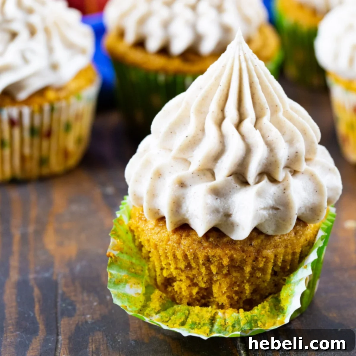 Pumpkin Cupcakes with Cinnamon Cream Cheese Frosting, wrapper pulled down, showcasing the moist interior.