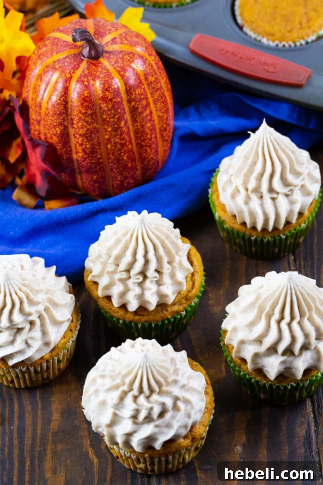 Pumpkin Cupcakes with Cinnamon Cream Cheese Frosting arranged on a tabletop with decorative pumpkins.