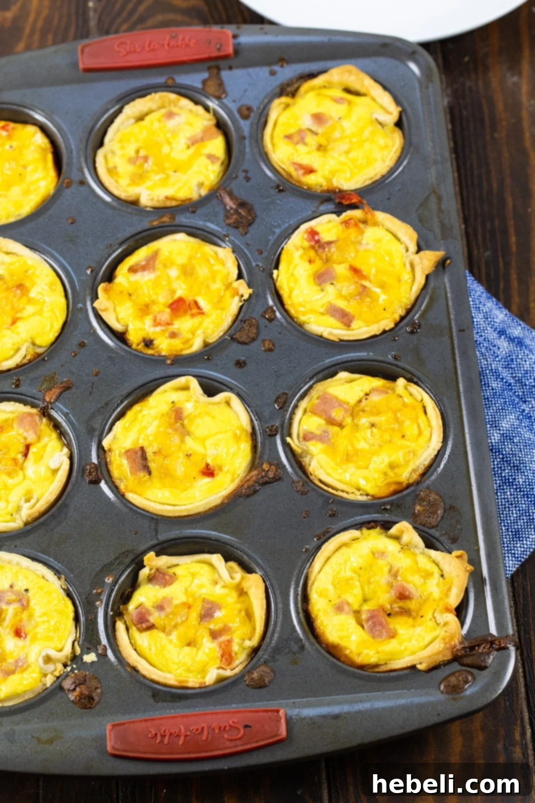 Several mini quiches baking in a muffin tin, showing their golden crusts and savory filling.