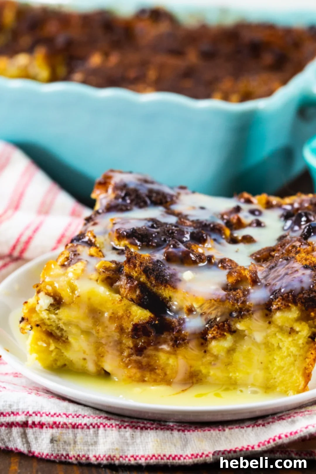 A delectable slice of White Chocolate Bread Pudding on a plate, generously drizzled with luscious white chocolate sauce.