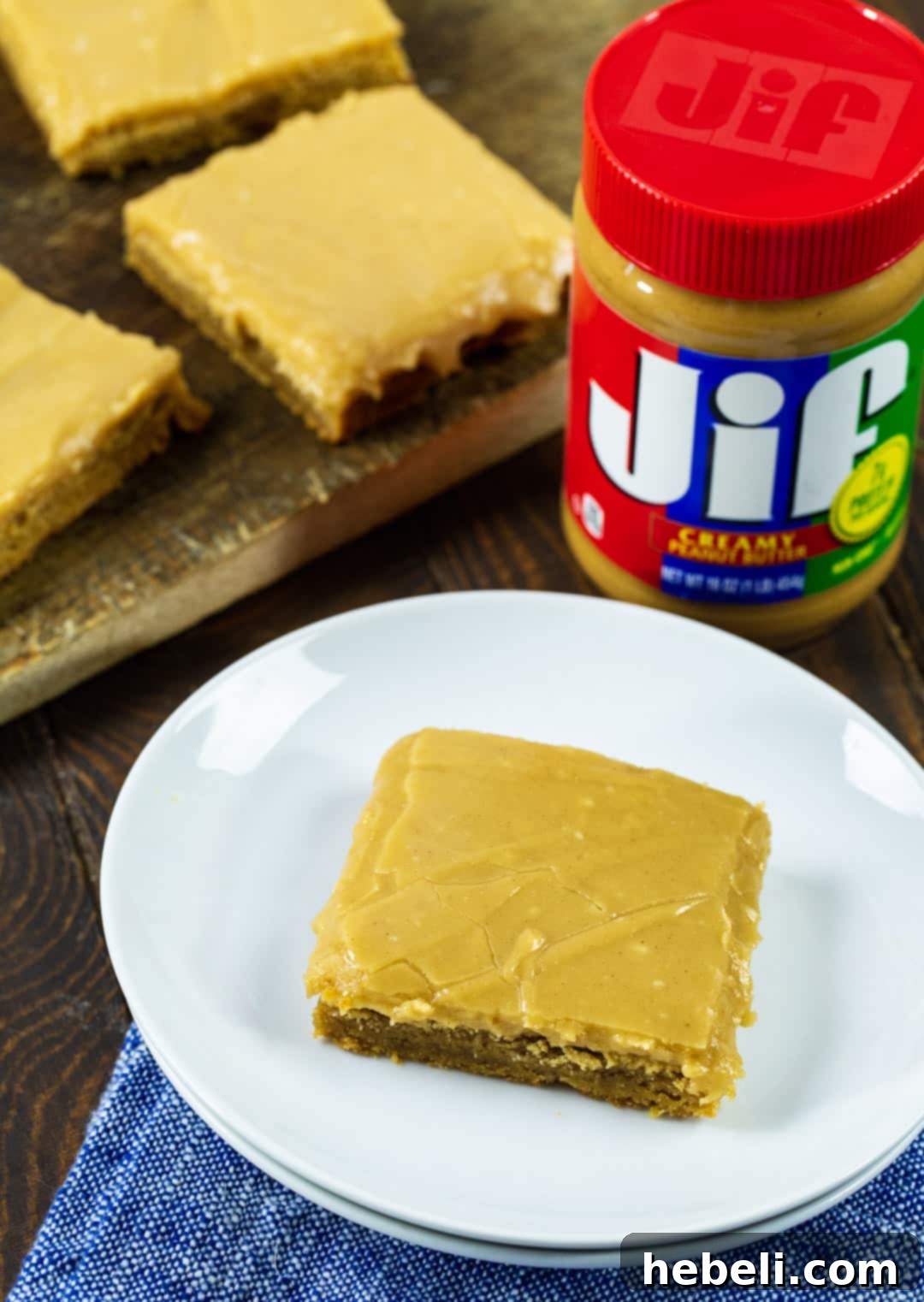 Decadent Peanut Butter Brownies 3 Two Peanut Butter Brownies alongside a jar of creamy peanut butter, highlighting the main ingredient.