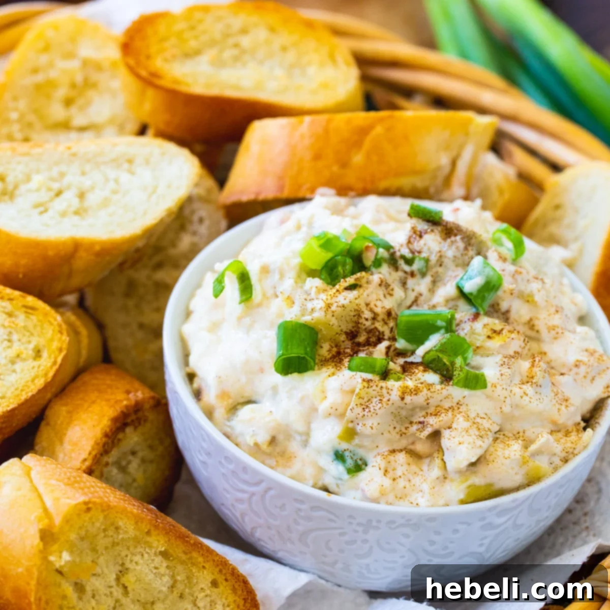 Crock Pot Crab Artichoke Dip in a ceramic bowl, surrounded by toasted baguette slices and fresh herbs.