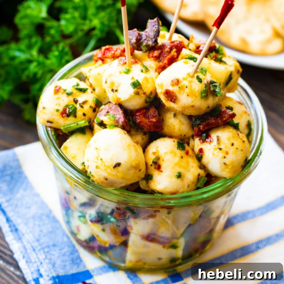 Spicy Marinated Mozzarella Balls in a clear glass bowl with toothpicks, garnished with herbs.