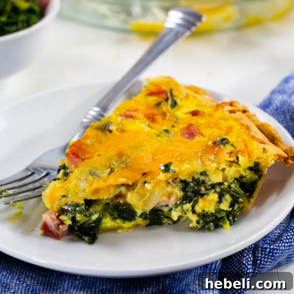 A perfectly baked slice of Southern Collard Greens Quiche, showcasing its vibrant green collards, bits of ham, and melted cheese, served on a white plate.