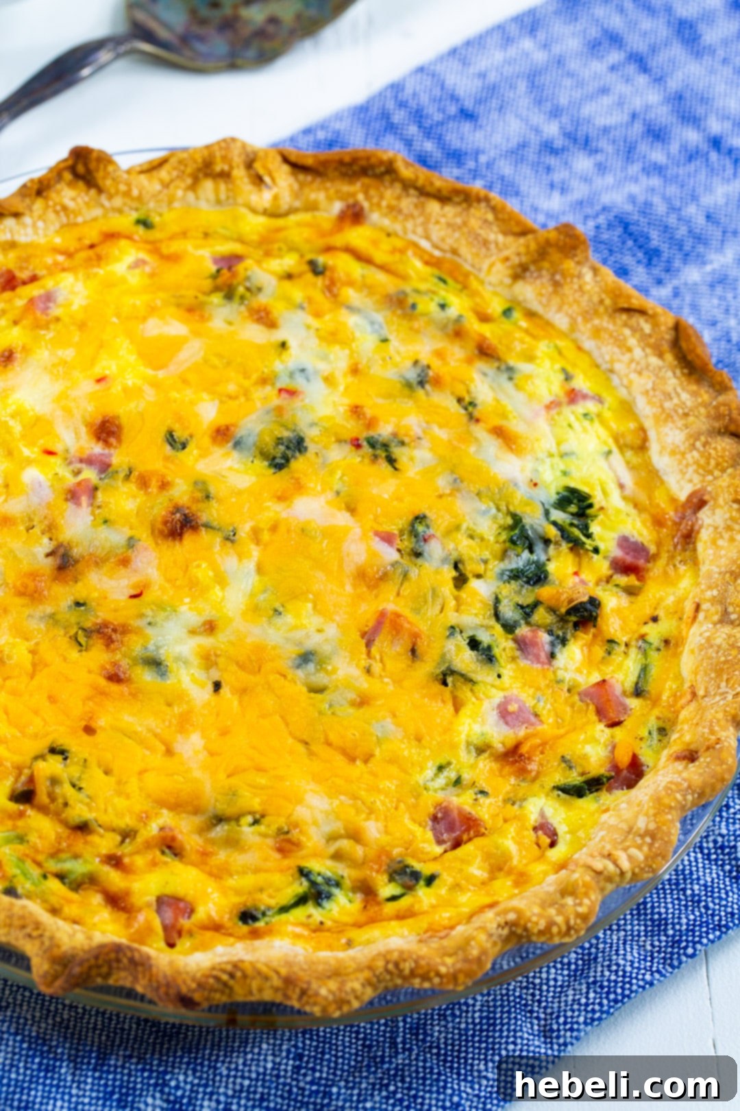 A stunning full view of a baked Southern Collard Greens Quiche, still in its pie pan, ready to be sliced. It's golden-brown with visible greens, ham, and cheese.