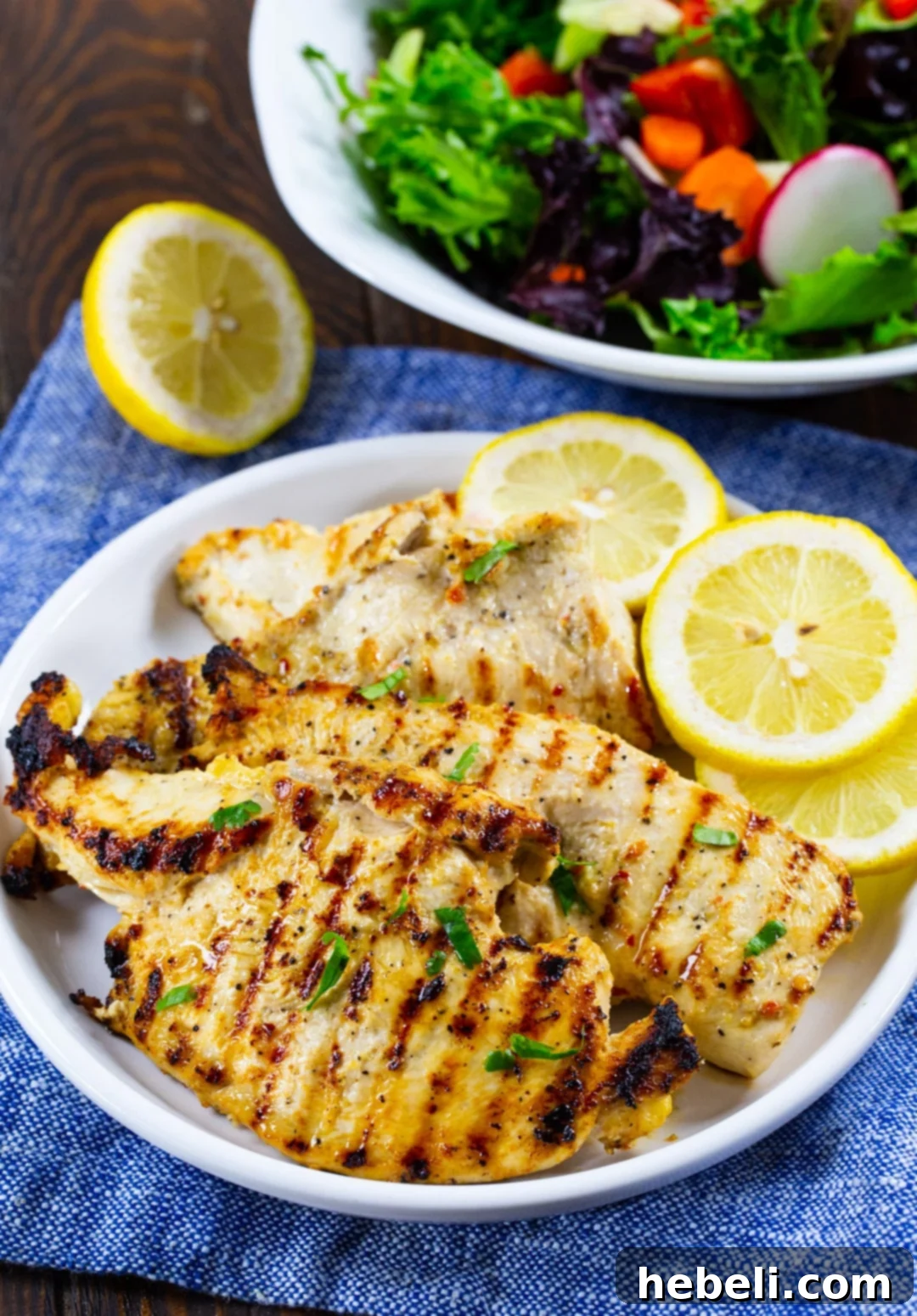 Perfectly grilled Italian Dressing Chicken, golden-brown with visible char marks, served on a white plate with fresh lemon wedges.