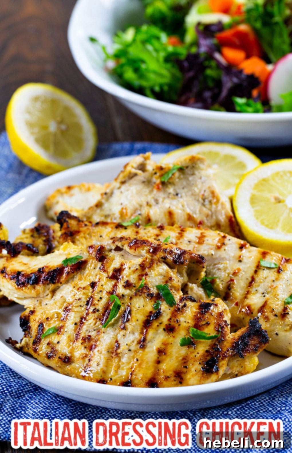A close-up of a serving plate featuring golden-brown Italian Dressing Chicken, garnished with fresh herbs and a lemon slice.