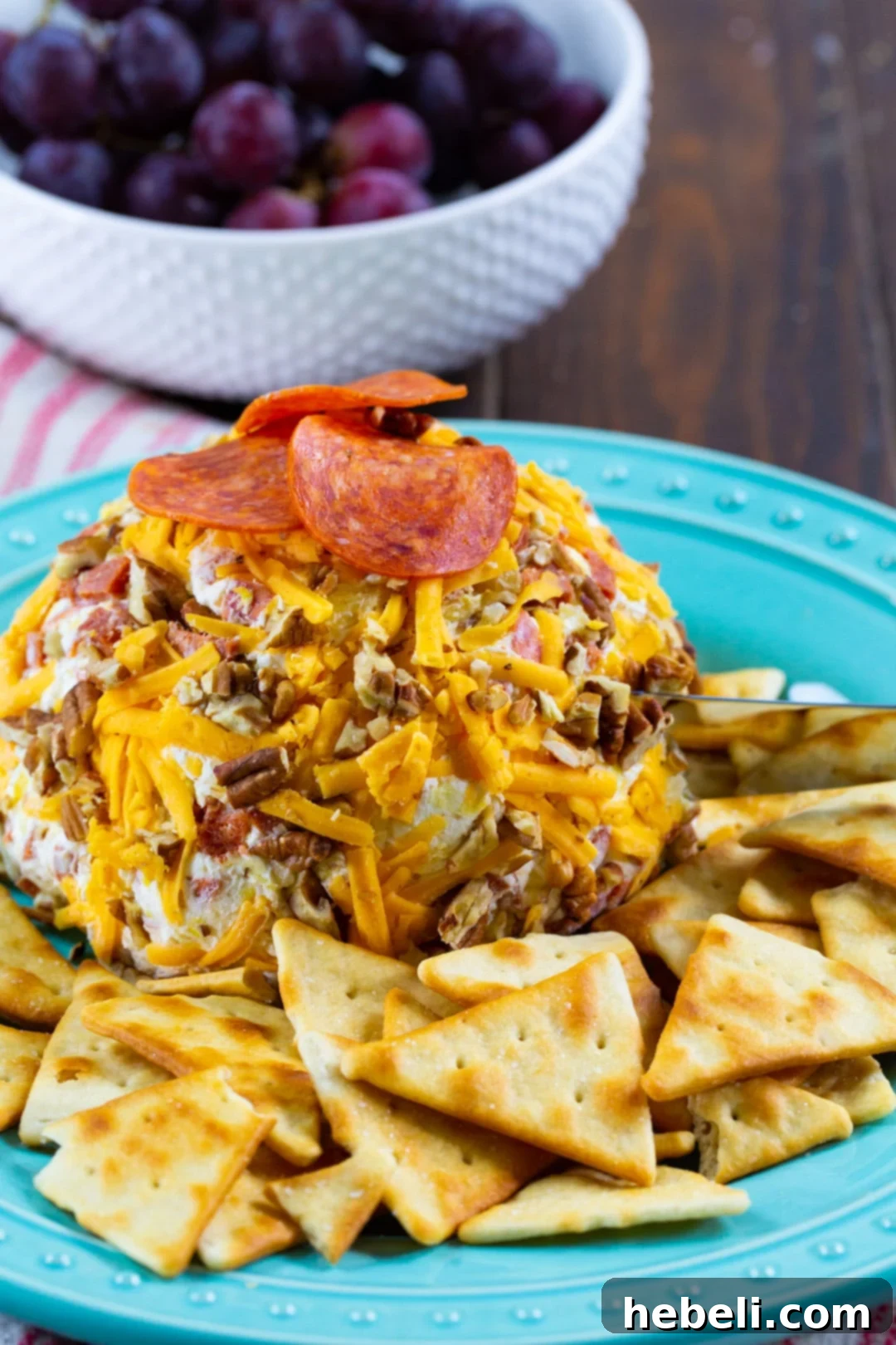 Loaded Pepperoni Cheese Ball 3 A beautifully presented Pepperoni Cheese Ball with an array of crackers and fresh grapes in the background.