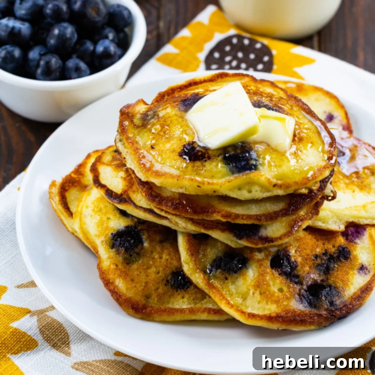A stack of golden brown Sour Cream Blueberry Pancakes generously topped with fresh blueberries, ready to be drenched in maple syrup.