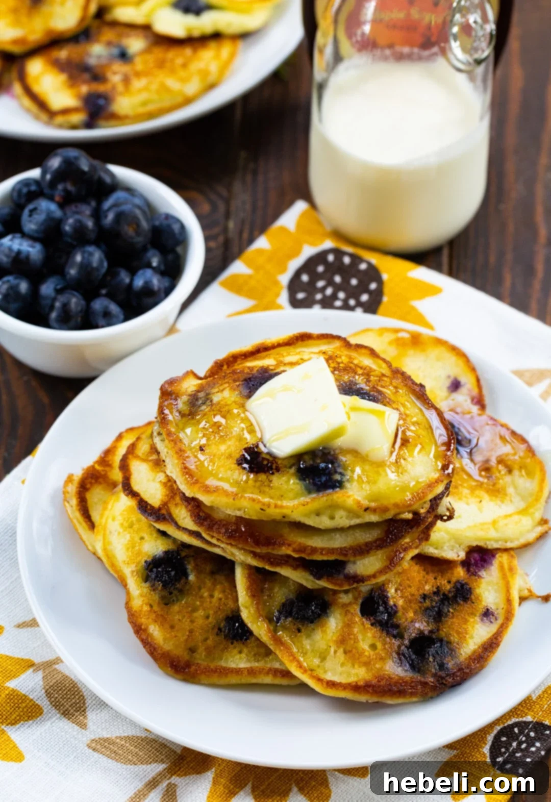 A rustic scene featuring a plate of freshly cooked pancakes, a bowl overflowing with vibrant blueberries, and a jug of milk, ready for a delicious breakfast.
