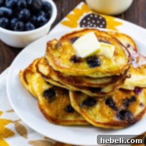 A close-up of a single Sour Cream Blueberry Pancake on a plate, showcasing its fluffy texture and embedded blueberries.