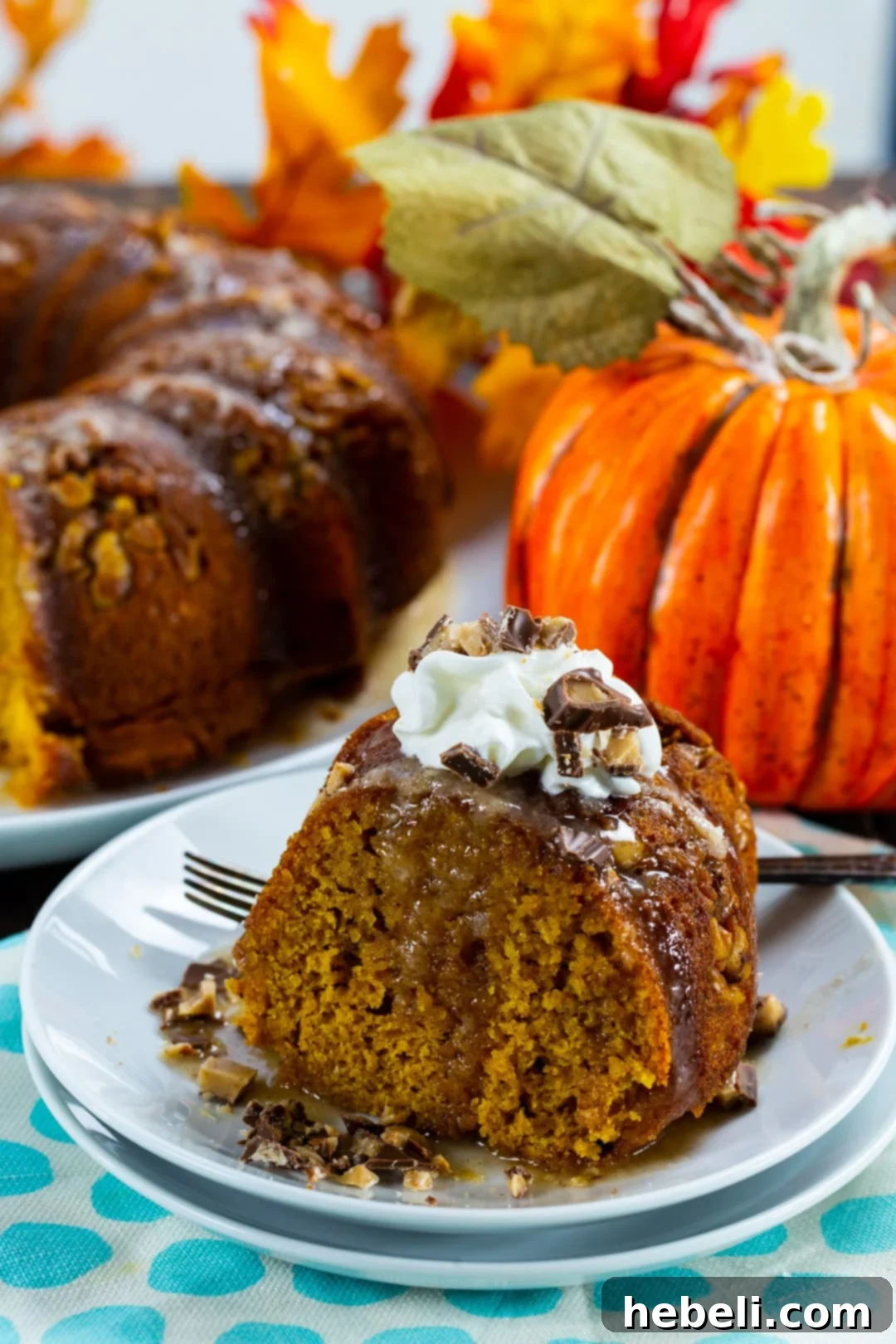 A large pumpkin bundt cake, still in its pan, with a piece removed to show the moist interior, surrounded by a festive fall setting.