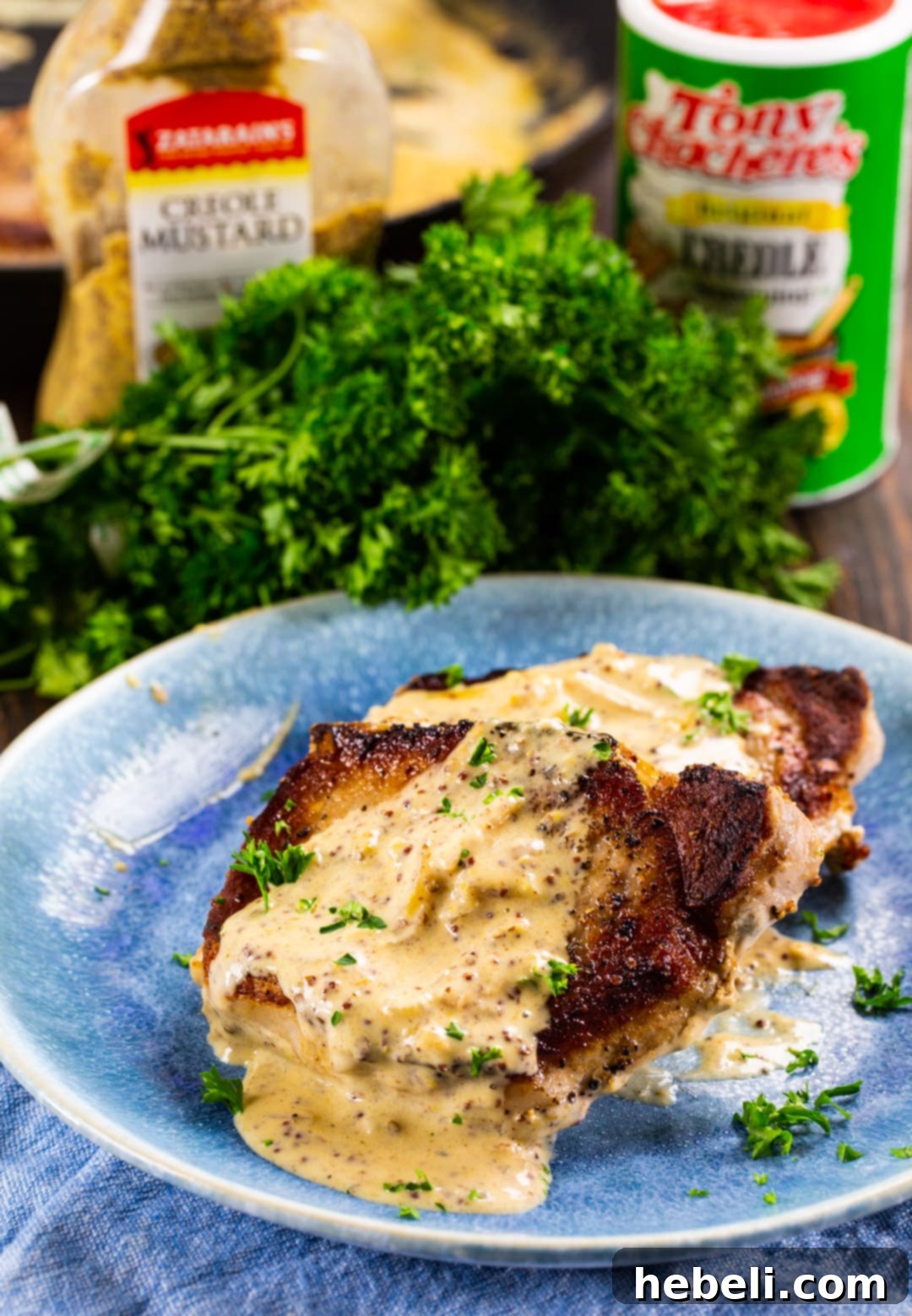 Two succulent Pork Chops with Creole Mustard Sauce plated with fresh parsley, emphasizing the rich sauce and tender meat.