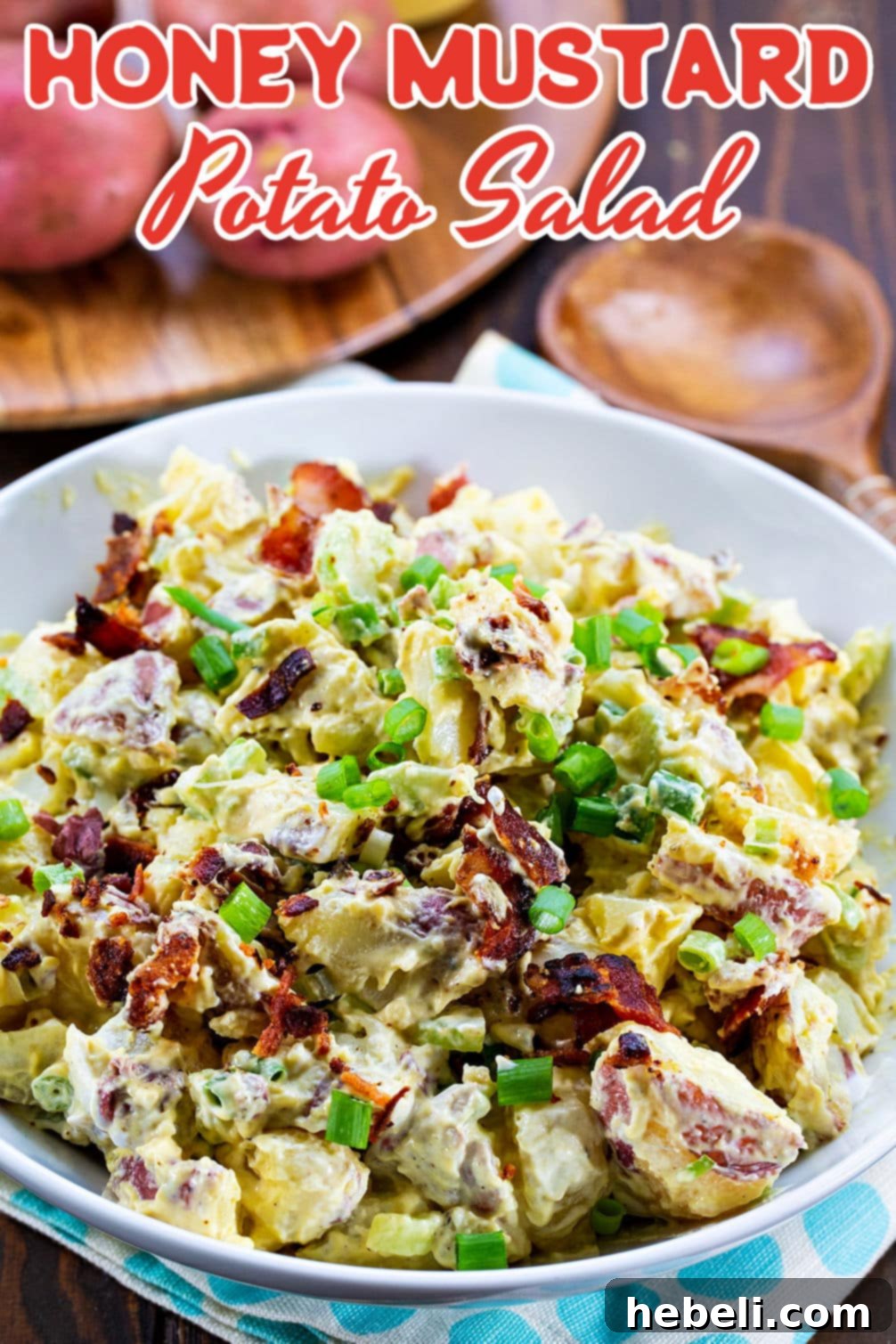 A bowl of Honey Mustard Potato Salad next to raw red potatoes, emphasizing the fresh ingredients.