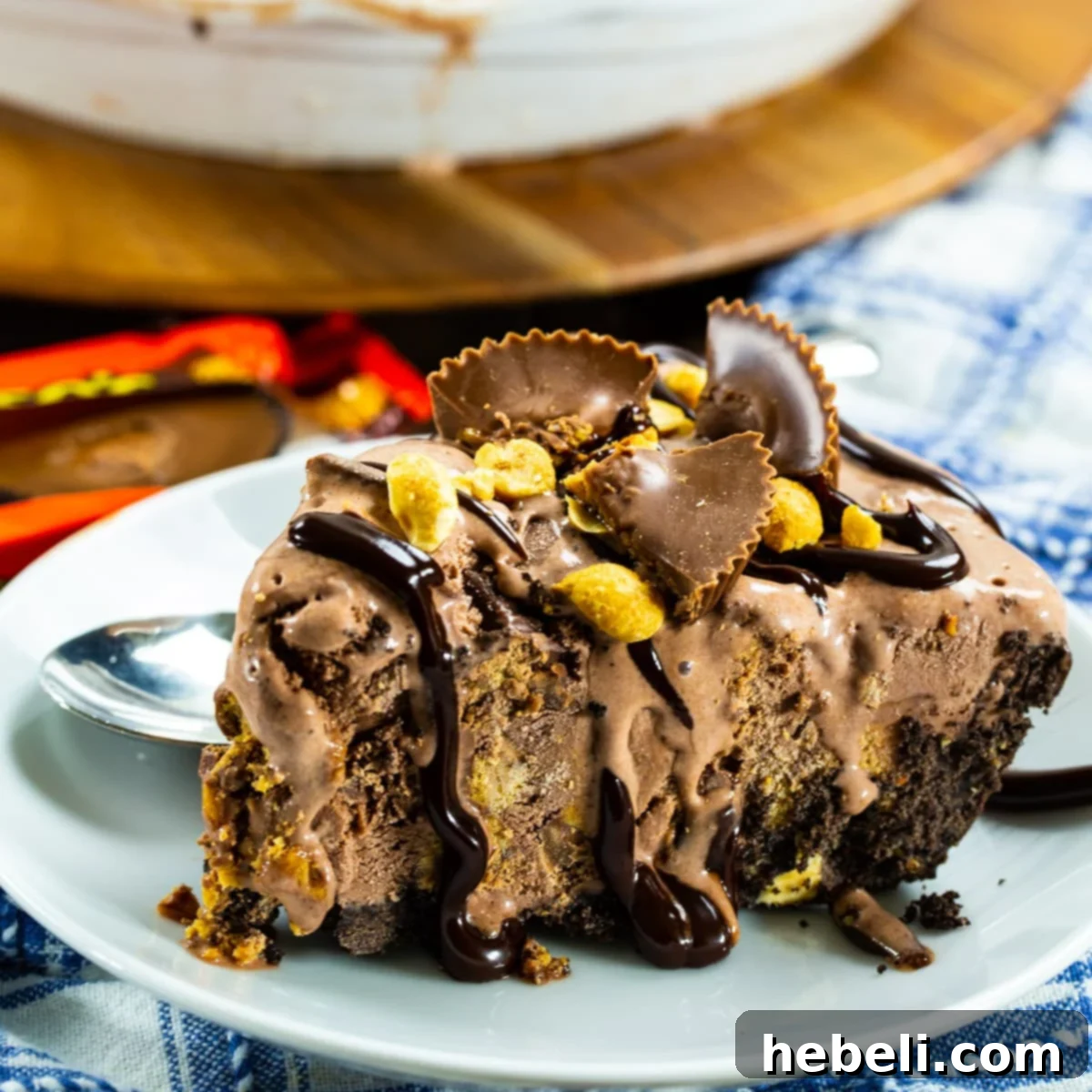 A perfectly sliced piece of Chocolate Peanut Butter Ice Cream Pie on a white plate, showcasing its layers of creamy chocolate ice cream, chunks of peanut butter cups, and a dark Oreo crust.