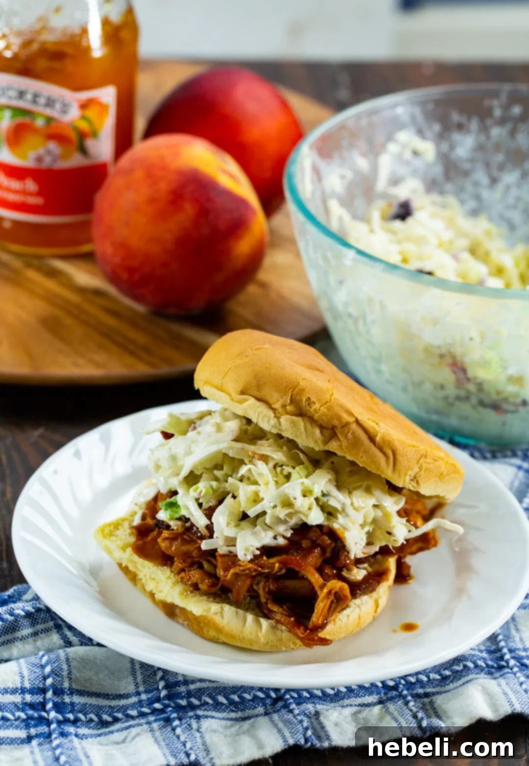 Slow Cooked BBQ Peach Pulled Chicken 4 Pulled Chicken Sandwich on a plate with peaches in background.