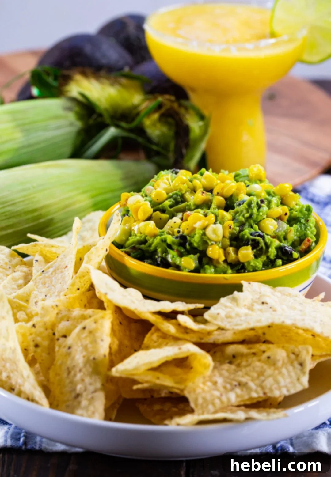 A vibrant plate featuring Black Bean and Corn Guacamole served with an array of tortilla chips, beside a refreshing margarita in the background.