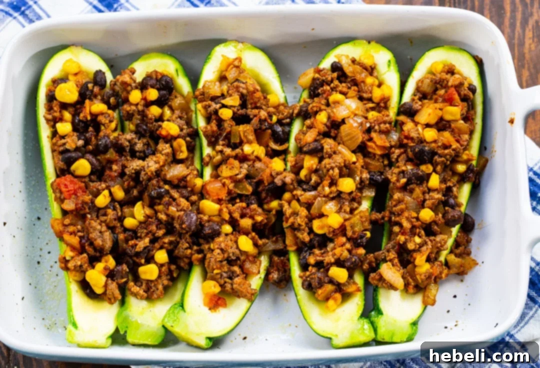 Zucchini boats generously filled with the cooked taco ground beef mixture, neatly arranged in a baking dish.