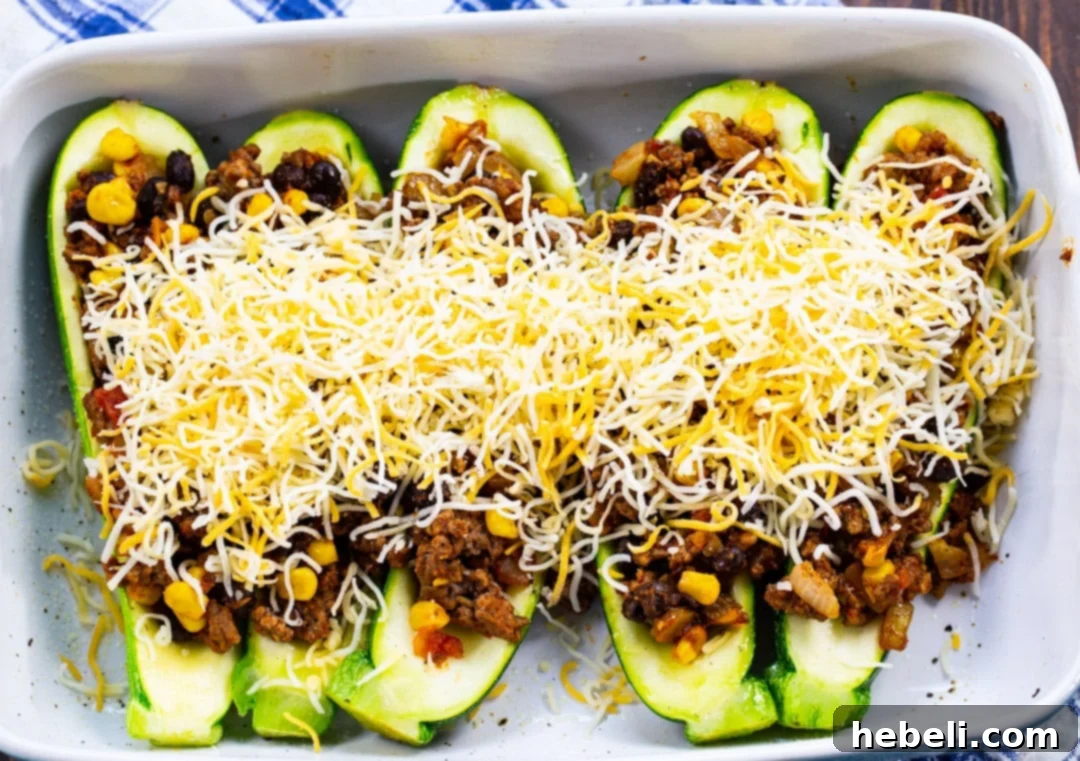 Shredded Mexican cheese blend generously sprinkled over the top of filled Taco Zucchini Boats, awaiting the oven.