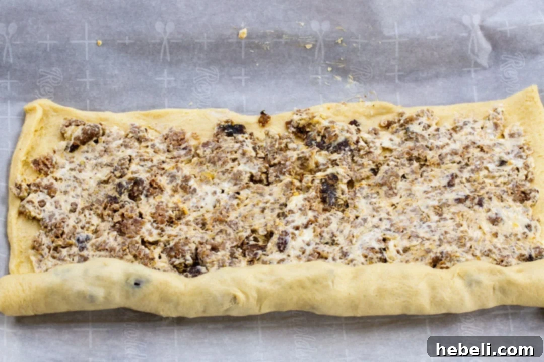 Hands carefully rolling up the crescent dough with the sausage and cream cheese mixture into a log.