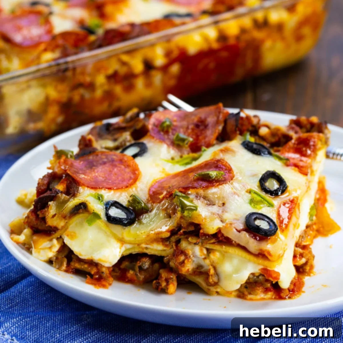 A delectable slice of Pizza Lasagna, showcasing its layers of cheese, pasta, and vibrant pizza toppings, served on a white plate, ready to be enjoyed.