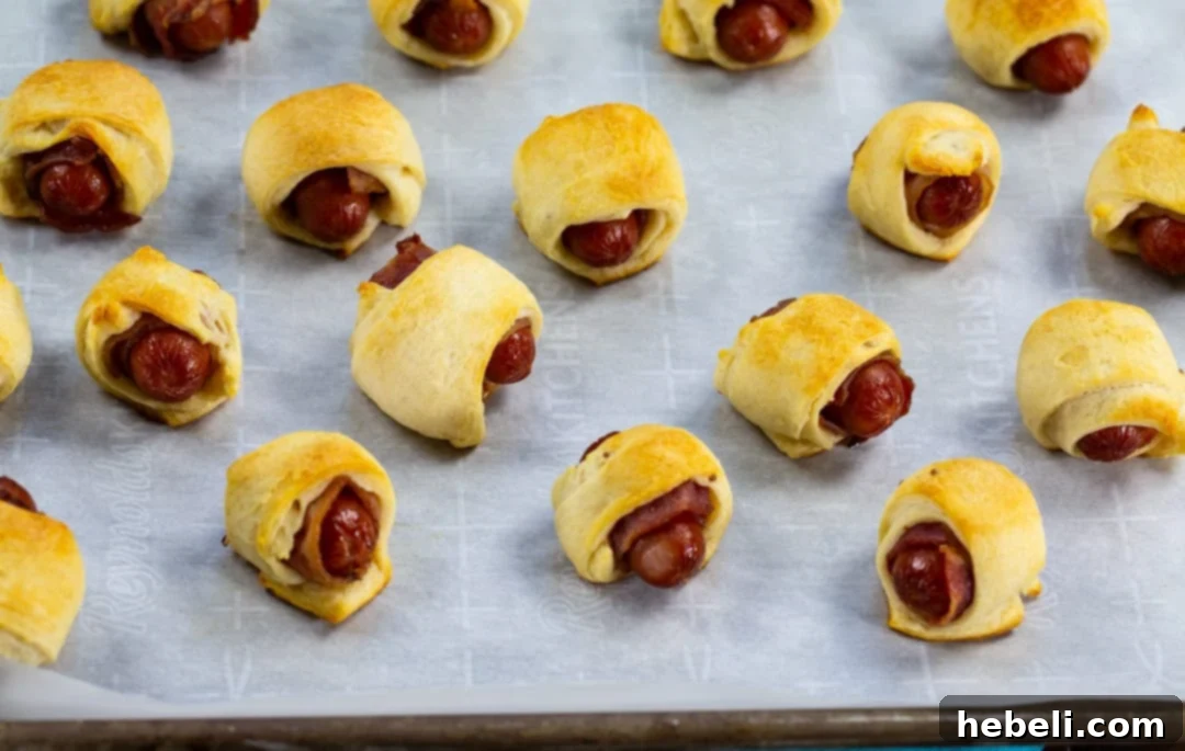 Bacon-Wrapped Sausage Bites 4 Bacon Pigs in a Blanket perfectly arranged on a parchment-lined baking sheet, golden brown and ready to be served hot.