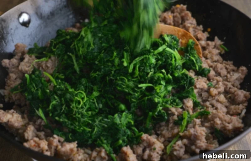 Savory Sausage and Spinach Swirl 5 Spinach being added and stirred into the cooked sausage and onion mixture.