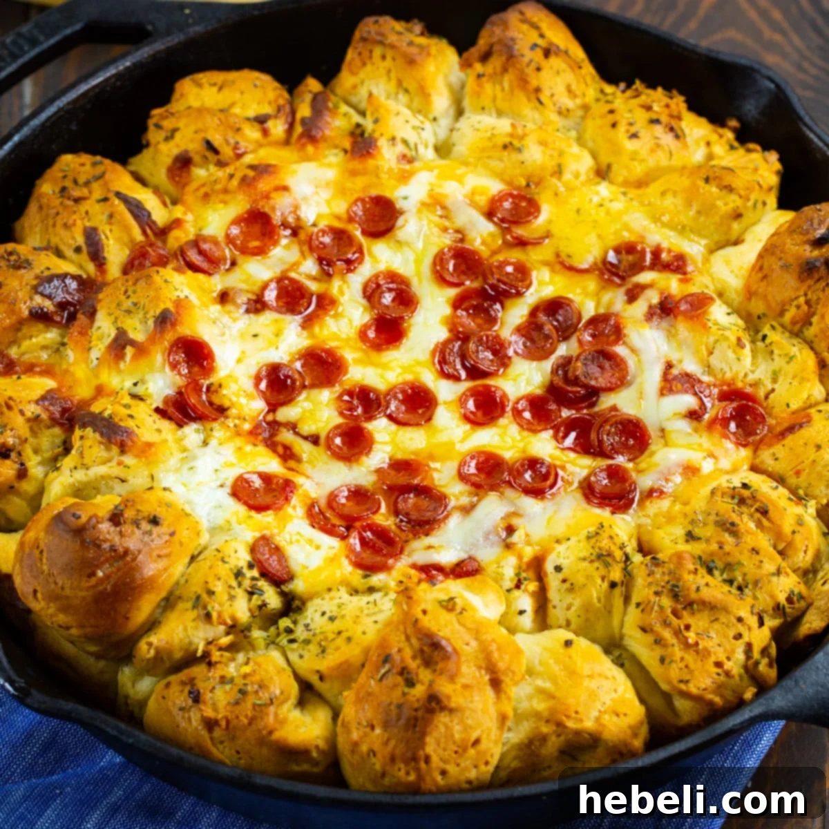 A golden-brown Pizza Dip Ring in a cast iron pan, bubbling with cheese and pepperoni, surrounded by perfectly baked biscuit balls.