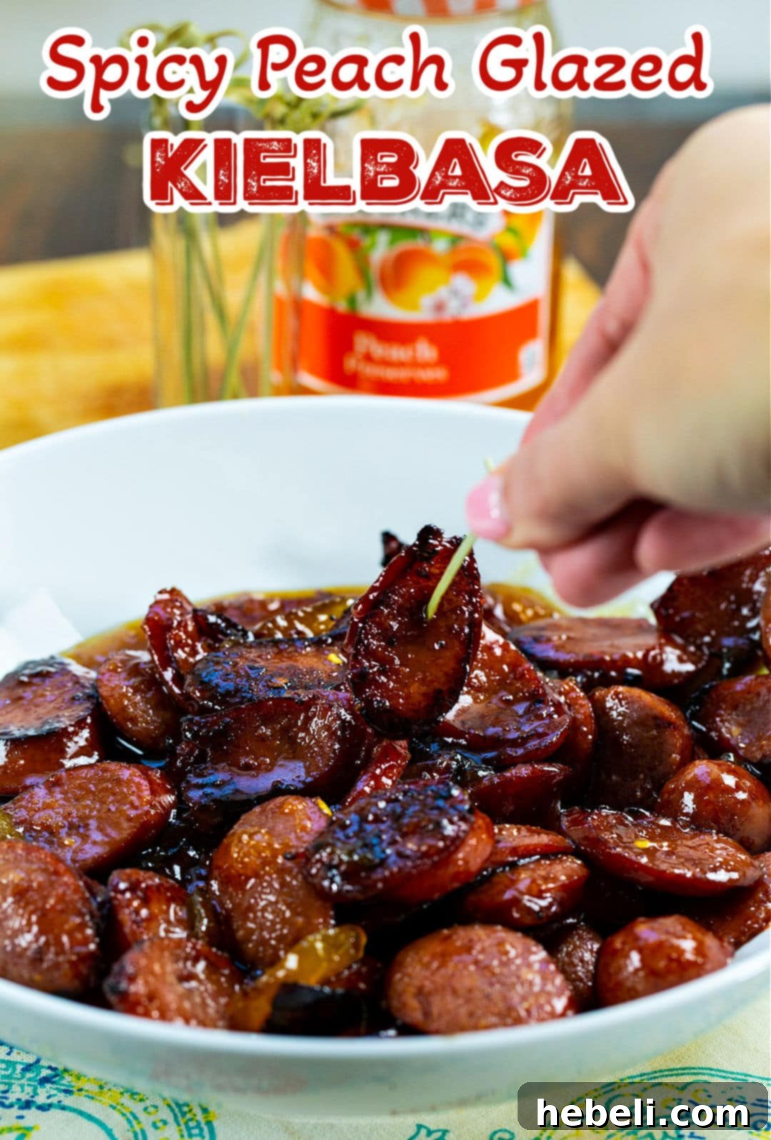 A close-up of a piece of Spicy Peach Glazed Kielbasa being picked up with a toothpick from a serving platter.