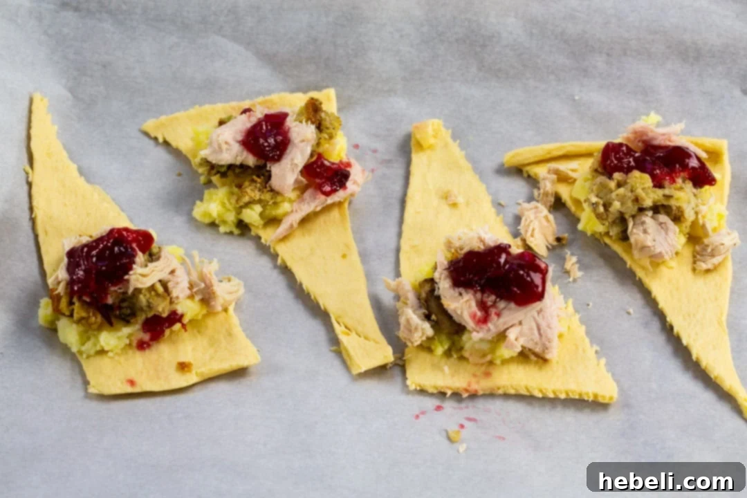 Delicious Thanksgiving Crescent Rolls 4 A close-up view of uncooked crescent dough triangles being prepared with spoonfuls of mashed potatoes, stuffing, turkey, and cranberry sauce before being rolled.