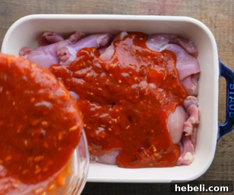 Sweet apricot glaze being poured generously over chicken thighs in a baking dish.