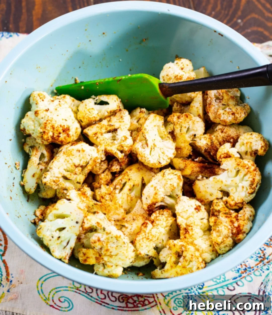 Fiery Cajun Cauliflower Bites 4 Raw cauliflower florets being tossed in a bowl with olive oil and a vibrant blend of Cajun spices, illustrating the seasoning process.