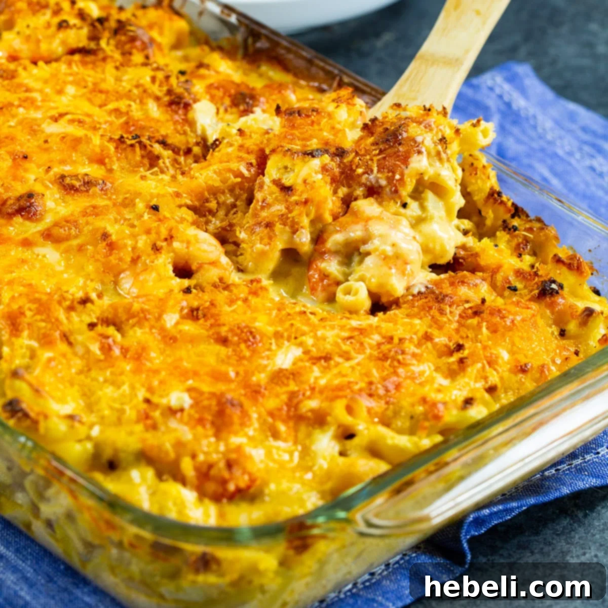 Wooden spoon scooping up a generous portion of golden-brown Cajun Shrimp and Crab Mac and Cheese from a baking dish.