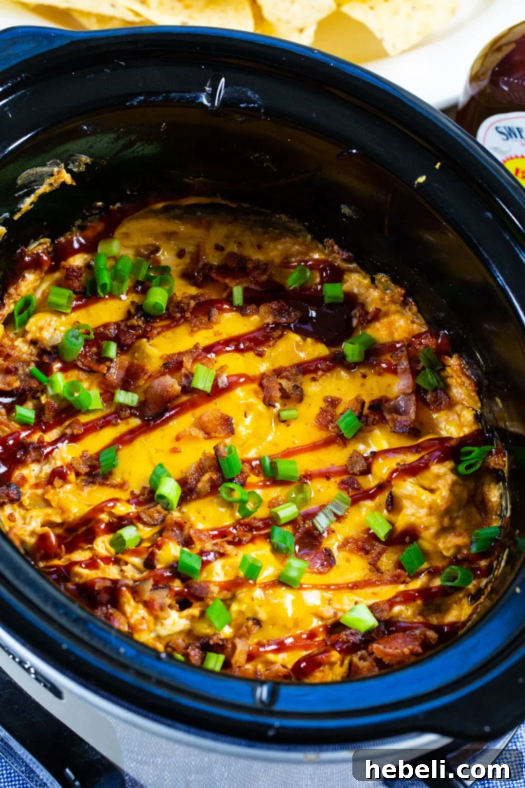 BBQ Chicken Dip in a slow cooker, being stirred to combine ingredients.