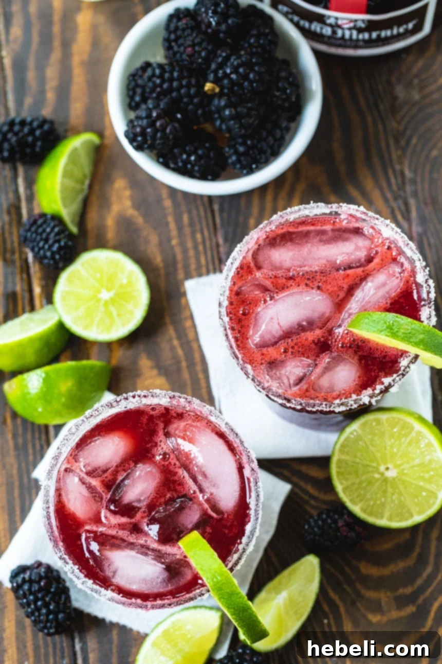 Overhead view of two Blackberry Margaritas, garnished with lime wedges and fresh blackberries scattered around.
