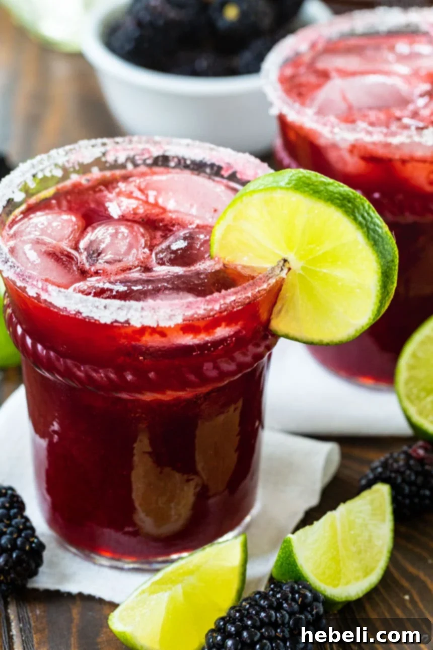 Close-up of a Blackberry Margarita in a salt-rimmed glass with a lime slice and fresh blackberries.