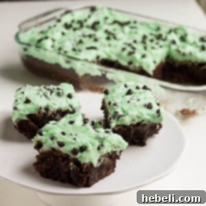 Close-up of fudgy brownies with green mint frosting and chocolate chips, ready to eat.