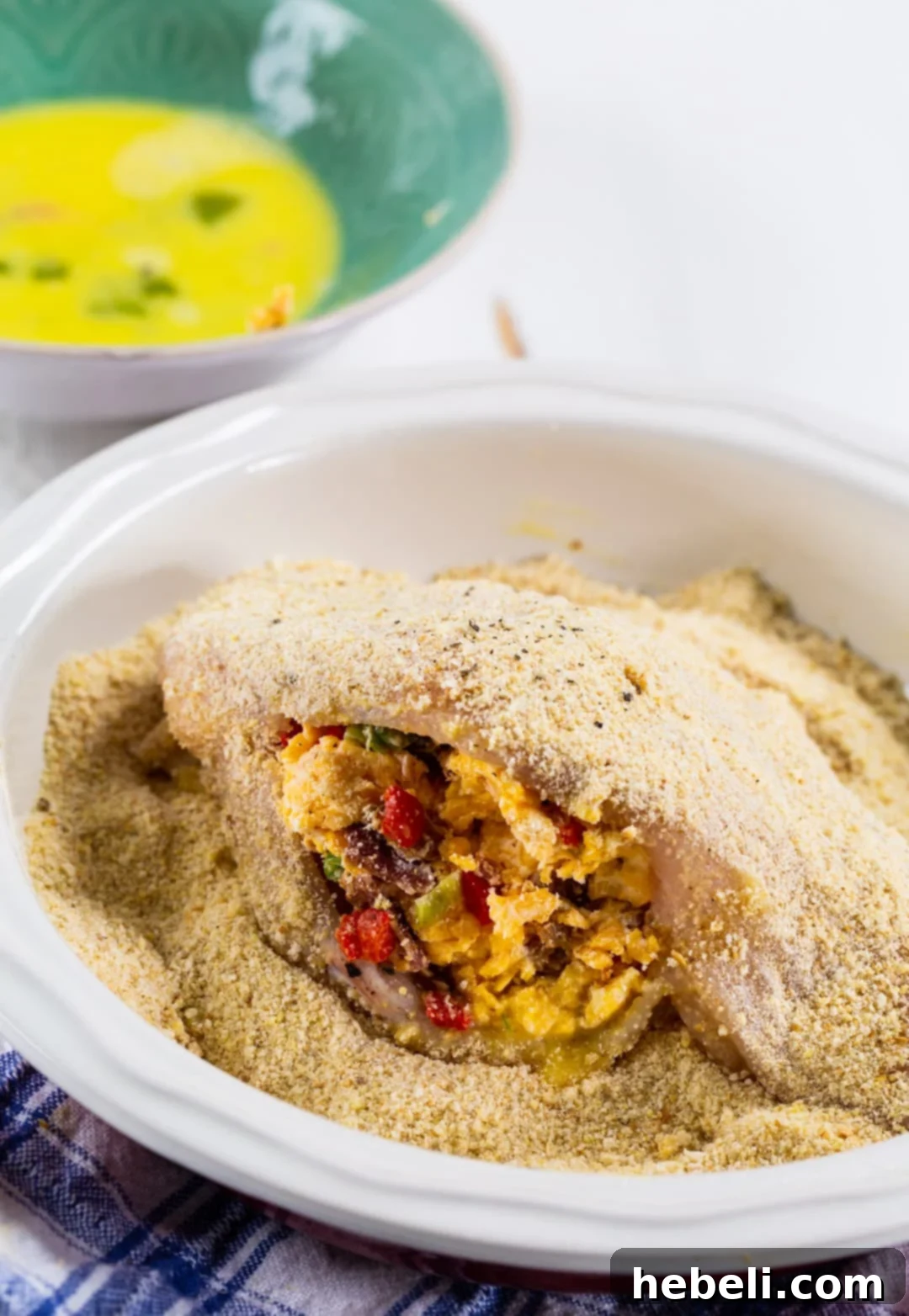 Creamy Pimento Cheese Stuffed Chicken 4 Chef hands coating a chicken breast with bread crumbs in a shallow dish, ready for cooking.