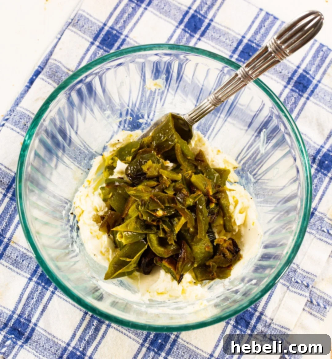 A mixing bowl filled with softened cream cheese and finely chopped roasted jalapenos, ready to be blended into the flavorful sandwich spread.