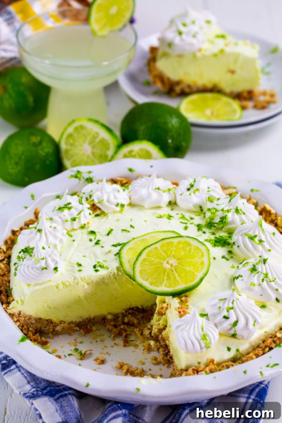 Effortless Margarita Dream Pie 4 No-Bake Margarita Pie beautifully garnished with fresh lime slices, with a glass of Margarita in the background.