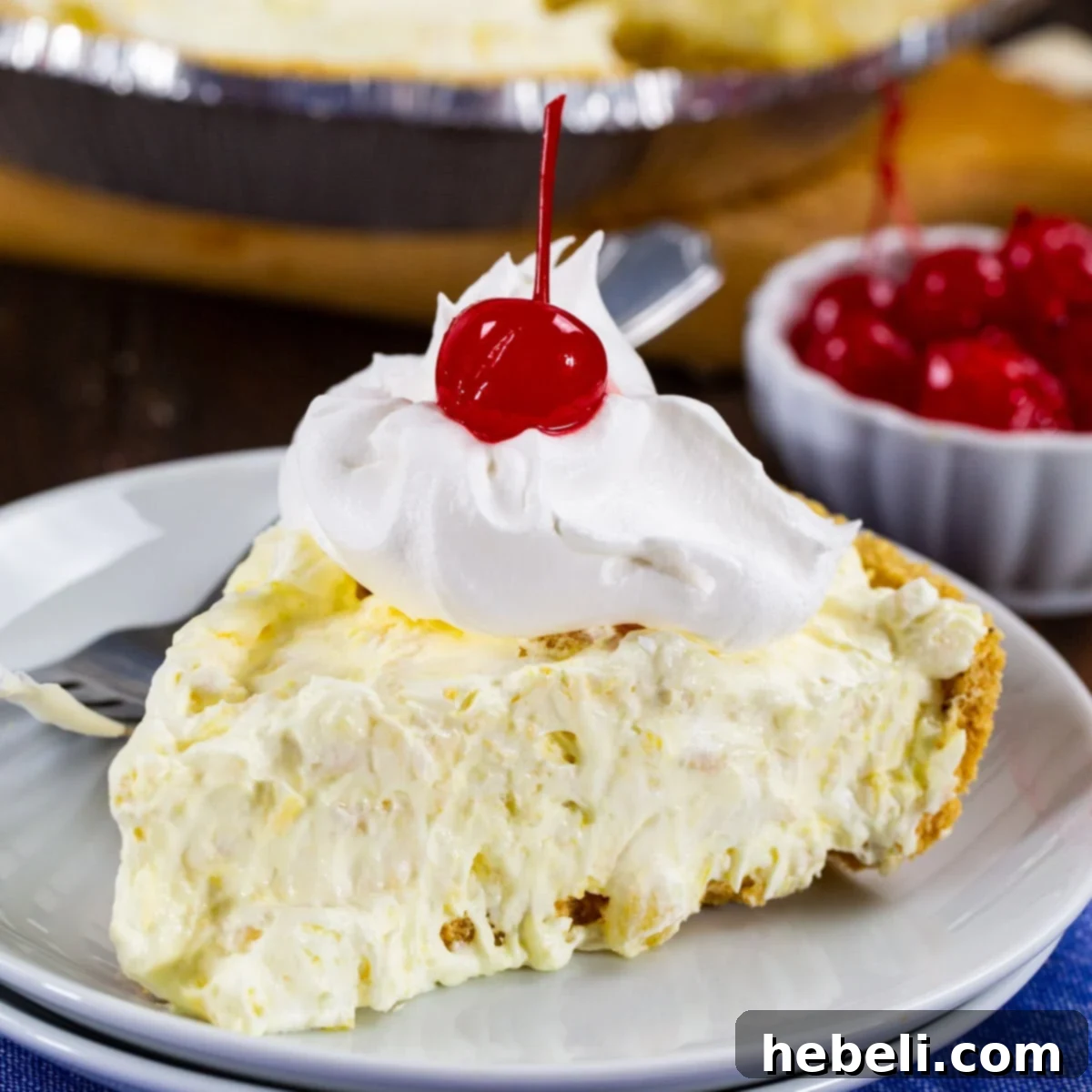 A beautifully presented slice of Pineapple Fluff Pie on a pristine white plate, garnished with a dollop of whipped cream and a bright red maraschino cherry.