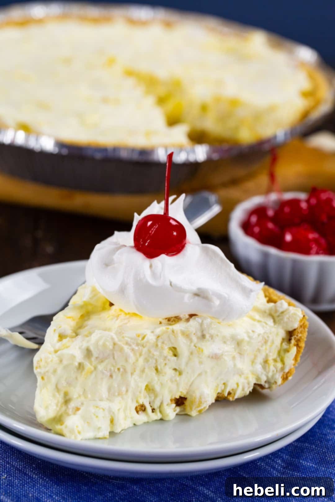 A close-up shot of a single slice of Pineapple Fluff Pie, showing its creamy texture and the golden graham cracker crust, set against a rustic background.