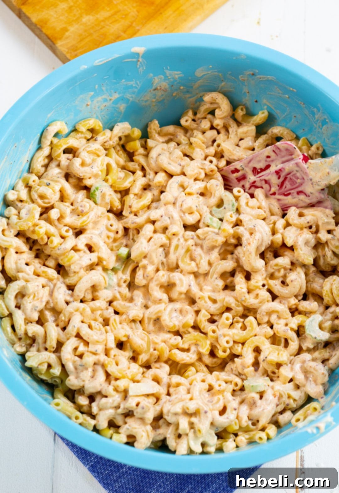 Kickin' Cajun Macaroni Salad 4 Prepared macaroni salad being mixed in a large bowl, showing the even distribution of ingredients and dressing.