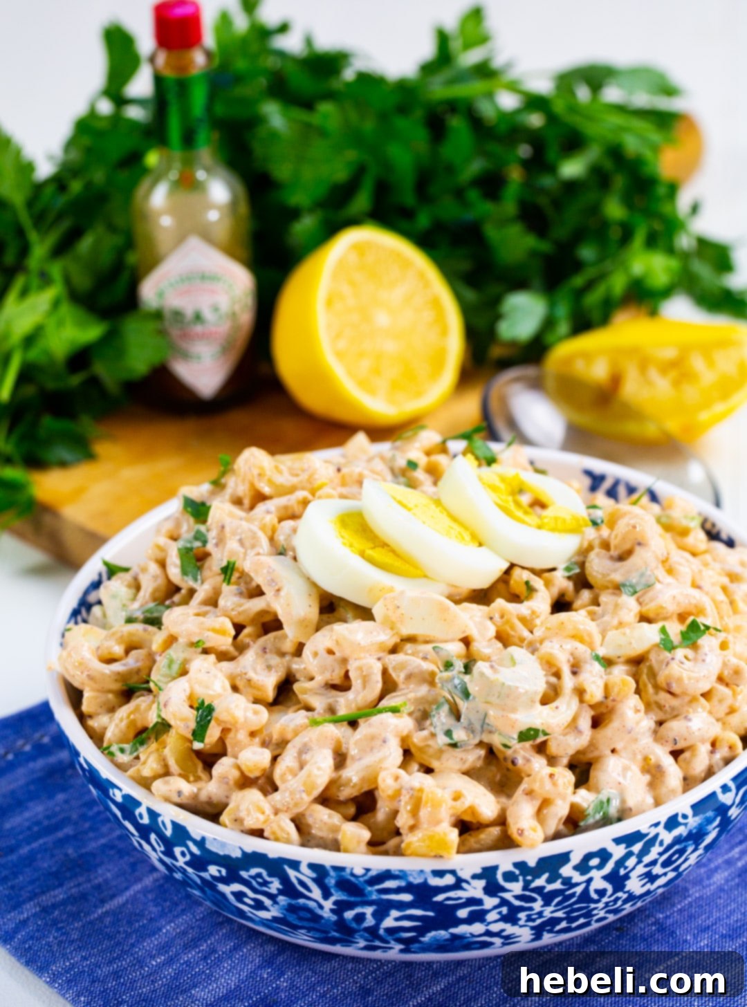 Kickin' Cajun Macaroni Salad 5 Cajun Macaroni Salad served in a white bowl, garnished with fresh parsley, with lemon slices in the background.