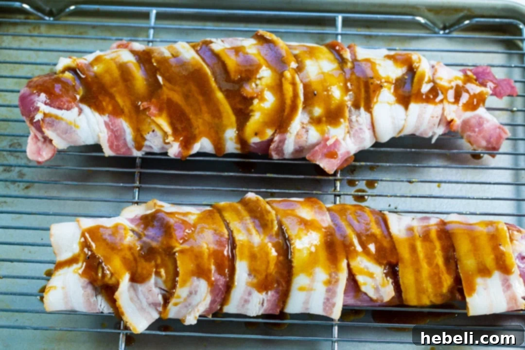 Two raw pork tenderloins expertly wrapped in strips of bacon, ready for the oven.