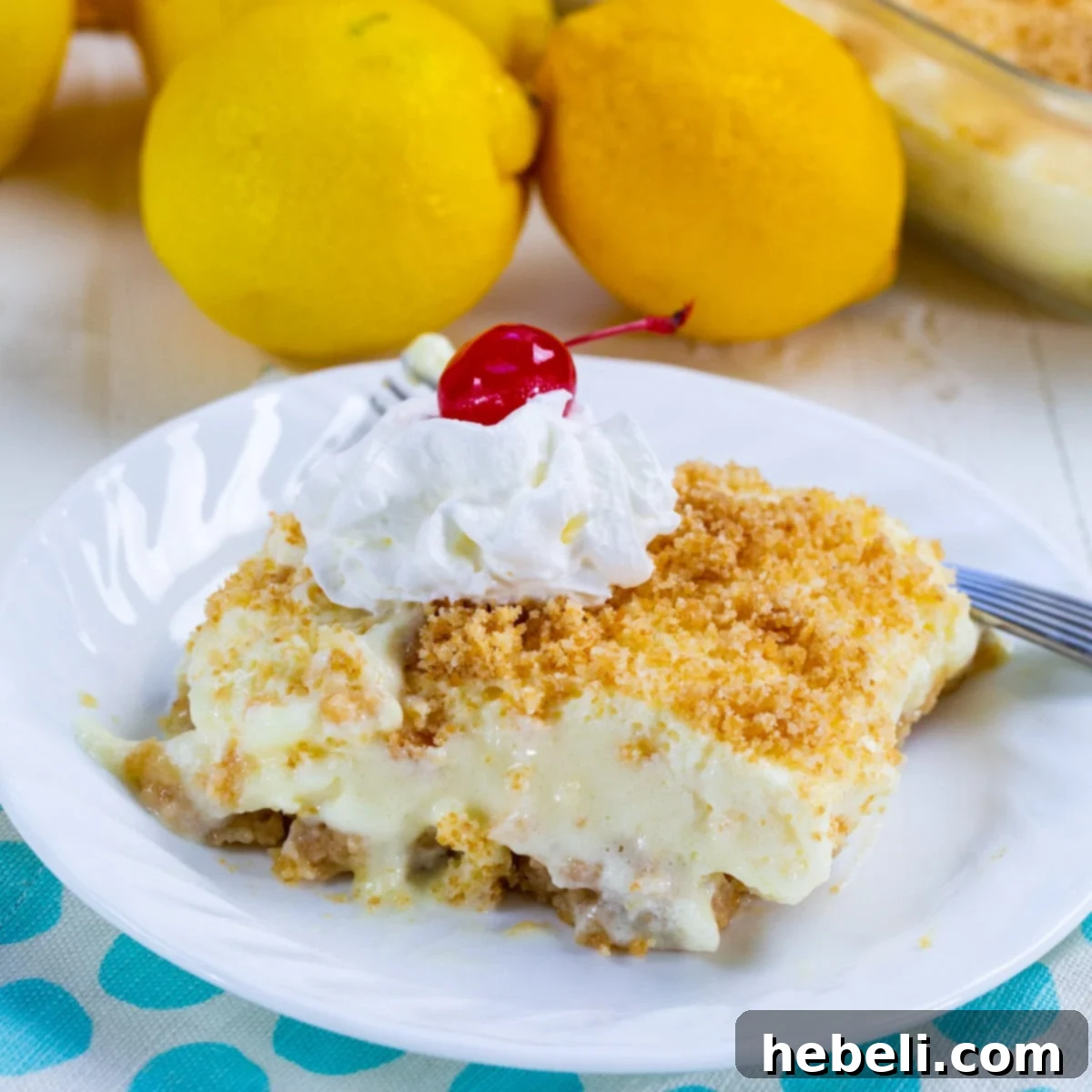 A beautiful slice of No-Bake Lemon Fluff dessert topped with fluffy whipped cream and a bright red cherry, served on a white plate, highlighting its light texture.