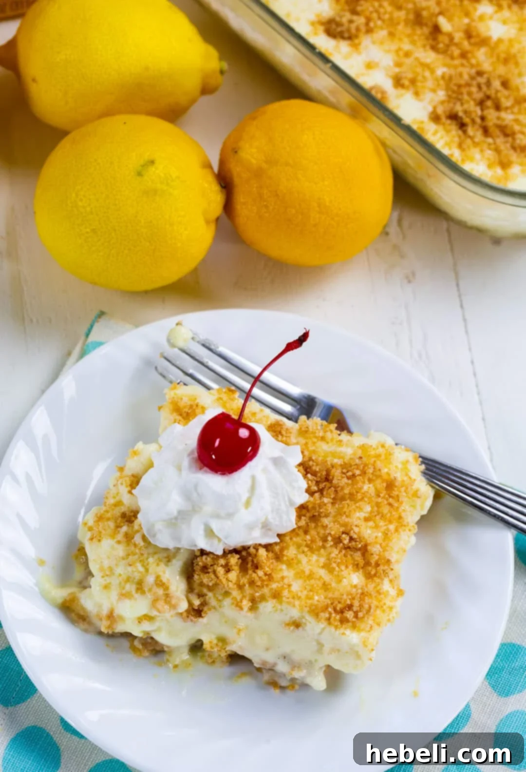 A close-up view of a perfect slice of Lemon Fluff, elegantly topped with a swirl of whipped cream and a glistening maraschino cherry, served on a plate.