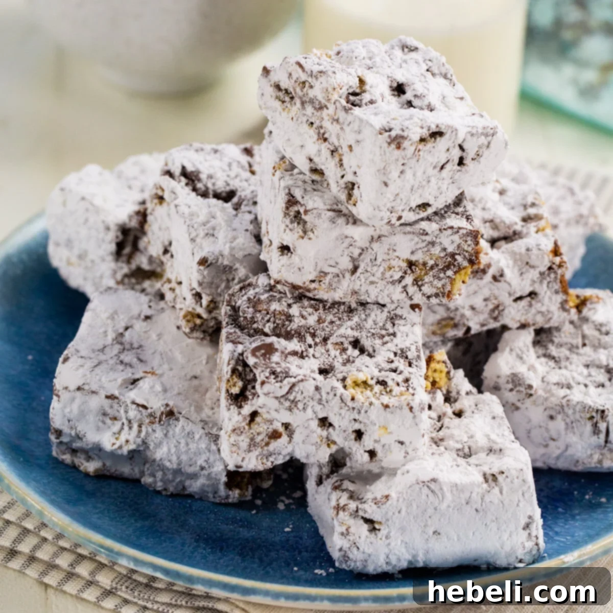 Muddy Buddy Bars stacked up on a plate, showcasing their powdered sugar coating and chewy texture.